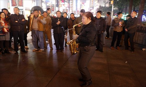 A busker plays a saxophone and dances to the music, attracting a crowd of onlookers. Photo: Cai Xianmin/GT