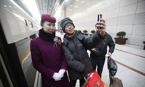 A passenger uses his mobile phone to take a group photo with a stewardess before boarding bullet train G801 to leave for Guangzhou, capital of south China's Guangdong Province, at the Beijing West Railway Station in Beijing, capital of China, Dec. 26, 2012. The world's longest high-speed rail route linking Beijing and Guangzhou started operation on Wednesday. Running at an average speed of 300 kilometers per hour, the 2,298-kilometer new route will cut the travel time between Beijing and Guangzhou from more than 20 hours to around eight. Photo: Xinhua
