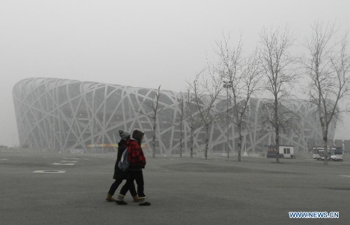 Citizens walk past the fog-enveloped National Stadium, or the 