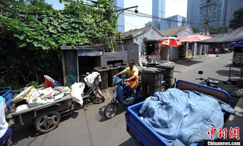 A man hauls garbage cans in his three-wheel electric bicycle through an alley. Photo: Jin Shuo/chinanews.com 