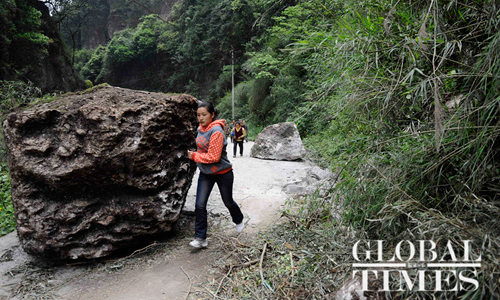 A local resident in Daxi town, Baoxing county, passes by a boulder displaced during the 7.0-magnitude quake, which jolted neighboring Lushan county in Sichuan Province at 8:02 am on Saturday. The quake caused at least 26 deaths and injured 2,500 others, with 30 in critical condition, in Baoxing, according to the county chief Ma Jun on Sunday morning. Photo: Li Hao/GT