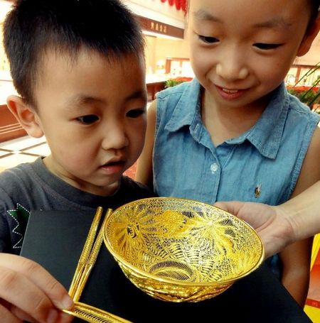Two children look at a set of gold tableware at a gold store in Jinan, capital of east China's Shandong Province, August 20, 2012. The set of tableware sells at 14,000 RMB ($2200). Photo: Xinhua
