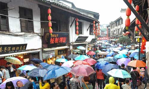 Tourists go sightseeing in the rain on a crowded road in Ciqikou, a millennium town, in southwest China's Chongqing Municipality, Oct. 02, 2012. With the coming of the National Day Holiday, Ciqikou saw a peak tourist season as thousands of tourists from home and abroad arrived here. Photo: Xinhua