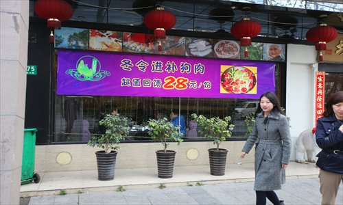 A woman passes by a restaurant in Xuhui district advertising a dog meat dish for 28 yuan. Photo: Cai Xianmin/GT