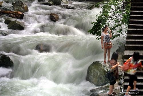 A visitor poses for photos next to a waterfall within the Fanjing Mountain, a natural scenic spot as well as a Buddhist sacred land, in Tongren, Southwest China's Guizhou Province, July 25, 2012. Photo: Xinhua

