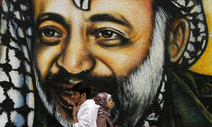 Palestinians walk in front of a mural of late Palestinian leader Yasser Arafat in Gaza City on Tuesday. The body of Arafat was exhumed, eight years after his death, as part of an investigation into allegations he was poisoned. Photo: AFP