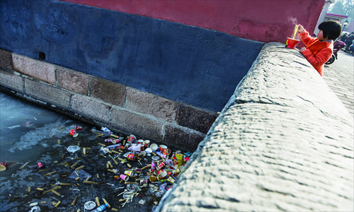 A girl eats instant noodles beside the moat of the Forbidden City. The moat has become a garbage dump. Photo: Li Hao/GT