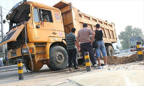 Passers-by look at a truck which overturned, spilling its load and burying a female cyclist early Sunday. The driver said he was trying to avoid an electric bike.Photo: CFP