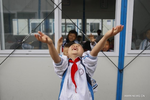 A student of the central primary school of Shangli Town enjoys the rain outside a makeshift classroom in Shangli, Lushan County, southwest China's Sichuan Province, May 16, 2013. The schoolhouses of the Shangli Town Center School were destroyed in the 7.0-magnitude earthquake taken place in Lushan on April 20, leaving more than 1, 200 students to have classes in newly built prefab houses. (Xinhua/Liu Xiao)&nbsp; 