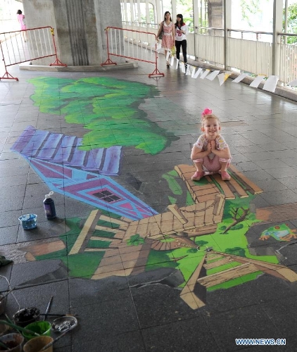 A girl poses for photos beside a street painting in Bangkok, Thailand, March 2, 2013. One local artist and 19 others from over the world feast the eyes of Thai people with their 3D and 4D street paintings during the Living Arts Festival held in Bangkok.(Xinhua/Gao Jianjun) 