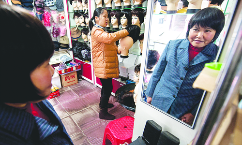Gu Aiqun tries a wig on at a local shop after losing all her hair during cancer treatment. Photo: IC