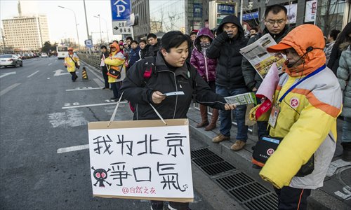 A volunteer hands a mask to a traffic warden at Xizhimen Wednesday. Photo: Li Hao/GT