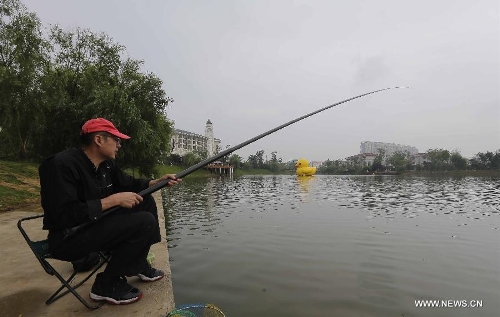 A man fishes near a mini rubber duck floating on a lake in the Hannan District of Wuhan, capital of central China's Hubei Province, June 1, 2013. The duck, made by a property company, is a mini copy of the huge rubber duck which appeared in Hong Kong, south China, on May 2. (Xinhua)&nbsp; 