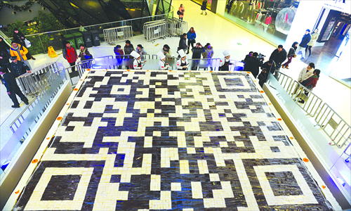 Consumers pass by a huge QD code-shaped cake in a shopping mall in Beijing. Taking photos of the code allows access to an Internet firm's services. Photo: CFP