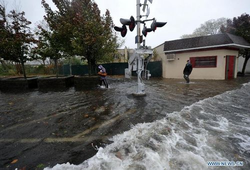 People walk in a flooded street at the Long Island in New York, the United States, on October 29, 2012. Hurricane Sandy, a massive storm described by forecasters as one of the largest ever that hit the United States, is making its way towards the population-dense East Coast. Michael Bloomberg, mayor of New York, has asked the public to stay at home when Sandy slams the city. Nearly 10,000 flights have been canceled for Monday and Tuesday by airlines bracing for Hurricane Sandy. Photo: Xinhua