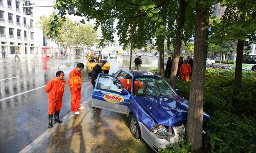 A police officer inspects a taxi that crashed into a tree while trying to dodge a moped Tuesday afternoon in Xuhui district. Three people were injured. Photo: Cai Xianmin/GT