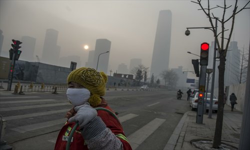 A cleaner wearing a mask crosses the road at Guanghua Lu in Chaoyang district Wednesday. The capital was severely polluted Wednesday, and meteorologists suggested residents stay at home. Photo: Li Hao/GT 