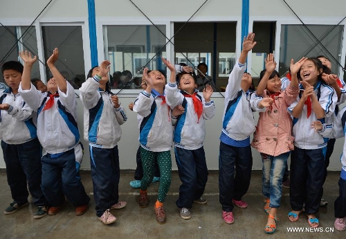 Students of the central primary school of Shangli Town enjoy the rain ouside a makeshift classroom in Shangli, Lushan County, southwest China's Sichuan Province, May 16, 2013. The schoolhouses of the Shangli Town Center School were destroyed in the 7.0-magnitude earthquake taken place in Lushan on April 20, leaving more than 1, 200 students to have classes in newly built prefab houses. (Xinhua/Liu Xiao) 