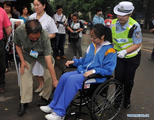 An examinee who has difficulties in walking is helped by a traffic police and a teacher as arriving to take the national college entrance exam at the Dongzhimen Middle School in Beijing, capital of China, June 7, 2013. Some 9.12 million applicants are expected to sit this year's college entrance exam on June 7 and 8. (Xinhua/Gong Lei)