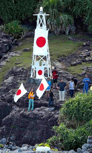 Japanese nationalists wave Japan's national flag in front of a lighthouse on one part of the Diaoyu Islands on Sunday. Around a dozen right-wing activists swam ashore from a 20-boat flotilla carrying activists and lawmakers, sparking strong protests from China. Photo: AFP 