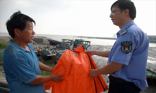A local fishery official in Jinshan district gives a free life jacket to a fisherman Tuesday to help him stay safe during typhoon season. Photo: Xinhua