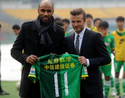 British soccer player David Beckham (R) is presented a jersey by Beijing Guo'an Soccer Club's footballer Frederic Oumar Kanoute in Beijing, capital of China, on March 21, 2013. Beckham visited the club as the ambassador for the youth football program in China and the Chinese Super League Thursday. (Xinhua/Gong Lei) 