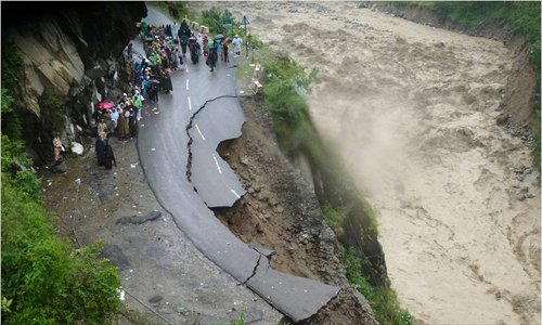 In this handout photograph released by the Indian army on Tuesday, Indian security personnel supervise residents and travelers as they stand on the remains of a flood damaged road alongside the River Alaknanda in Chamoli district in the northern Indian state of Uttarakhand on Tuesday.  Torrential rains and flash floods washed away homes and roads in north India, leaving at least 64 people dead and thousands stranded, as the annual monsoon hit the country earlier than normal, officials said. Photo: AFP