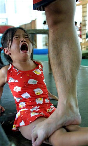 A girl cries as a coach stands on her legs to help stretch her ligaments at an amateur sports school in Nanning, Guangxi Zhuang Autonomous Region.
