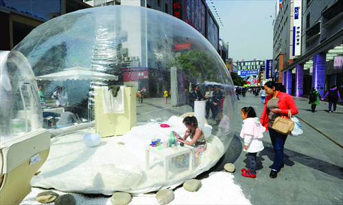 Pedestrians watch a woman living in a bubble room Sunday in Chengdu, Sichuan Province. A local hotel operator used the event to promote its bubble room services, which can be set up according to the client's specifications. The model will spend two days in the bubble. Photo: CFP