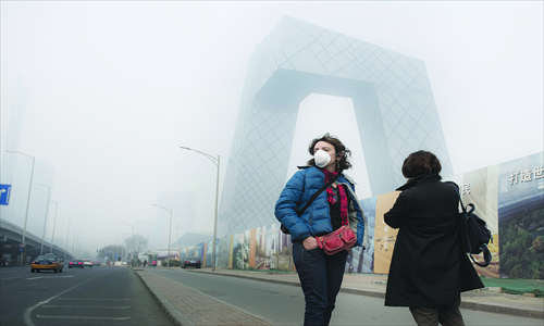 A woman wears a mask as she walks along the East Third Ring Road near the China Central Television Tower, Chaoyang district Sunday. Air pollution in the capital has again been high in recent days. Photo: Li Hao/GT