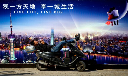 A man on a motorbike in the old street texts a message in front of a hoarding advertising a new residential complex. Photo: Cai Xianmin/GT