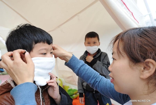 Resident Yang Xueping help her son to wear a mask at a temporary shelter site in Taiping Town of Lushan County in Ya'an City, southwest China's Sichuan Province, April 21, 2013. Several temporary shelter sites can be seen in Lushan County and the life supplies in these shelter sites are sufficient. A 7.0-magnitude earthquake jolted Lushan County on April 20 morning. (Xinhua/Li Jian)