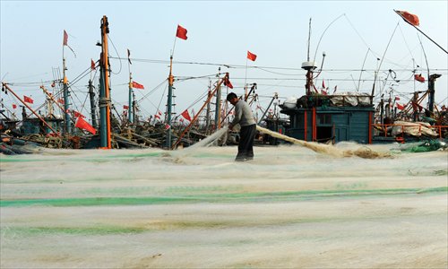A fisherman repairs trammel nets at a port in Qingdao, East China's Shandong Province Monday. The city's total output value of fishery and other marine products last year reached 42 billion yuan ($6.79 billion), up 5.5 percent compared with the previous year. The local government also set up a working target of helping its fishermen's per capita income to rise by 12 percent in 2013. Photo: CFP