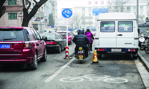 Riders try to squeeze past a police minivan which has parked on a cycle lane in Xidan, Xicheng district Wednesday. Photo: Li Hao/GT