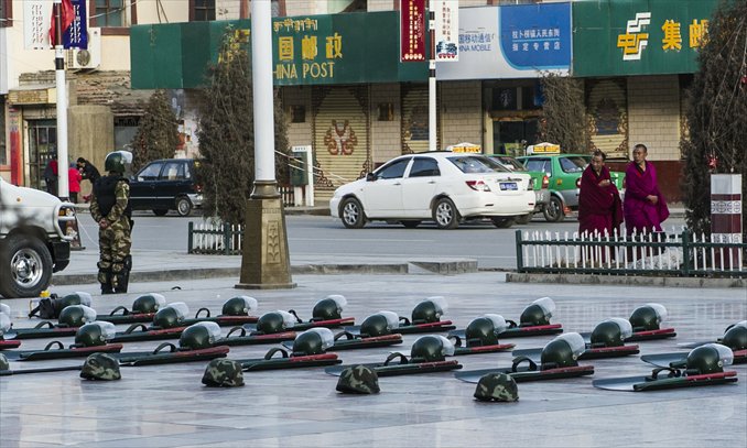 An armed police officer stands guard while two monks pass by in Xiahe, Gansu Province on March 7. Photo: Li Hao/GT