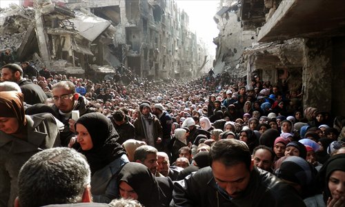 An undated handout picture made available on Wednesday by the United Nation Relief and Works Agency (UNRWA) shows Palestinian and Syrian residents of Yarmuk Palestinian Refugee Camp crowding into a destroyed street as food is distributed, in Damascus, Syria. Photo: CFP
