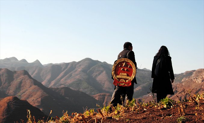 Two judicial workers, one carrying the national emblem on his back, walk along a mountain path. Photo: CFP