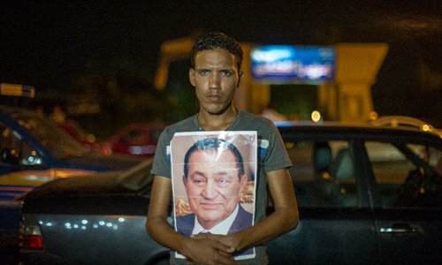 A man holds Egyptian ex-president Hosni Mubarak's photo standing outside the Maadi Military Hospital in Cairo, Egypt, June 20, 2012. Egypt's ex-president Hosni Mubarak was in a comma and relied on a respirator, a hospital source told Xinhua late Tuesday night, denying that he was 