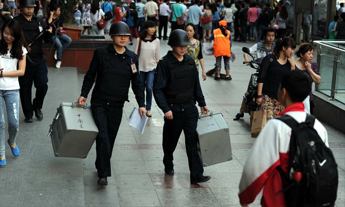 Two guards carrying a case walk through crowds while covered by an armed teammate. Photo: CFP