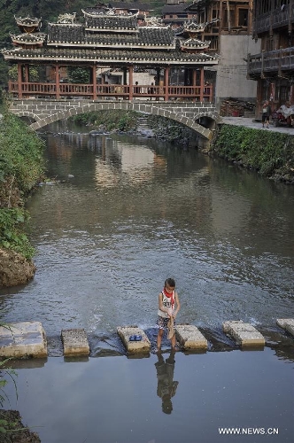 A child plays before a wind and rain bridge in Dimen Dong minority village in Liping County of southwest China's Guizhou Province, June 20, 2013. Dimen is a Dong minority village with about 2,500 villagers. It is protected properly and all the villagers could enjoy their peaceful and quiet rural life as they did in the past over 700 years. (Xinhua/Ou Dongqu)