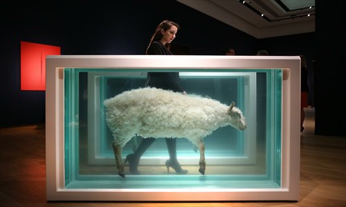 A Christie's employee walks between the two halves of Damien Hirst's Away from the Flock (Divided) piece ahead of its Post War and Contemporary art sale on February 8, 2013 in London, England. Photo: CFP
