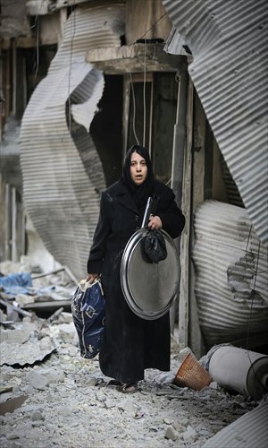 A Syrian woman carries goods from her apartment destroyed in an air strike by Syrian government forces in the northern city of Aleppo on Tuesday. Photo: AFP