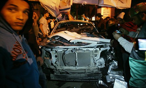 People stand around a police patrol car on Monday in Benghazi after its was hit by a bomb, injuring two policemen. The blast came two days after the Italian consul to Benghazi escaped unscathed from a gun attack while inside his armored vehicle in the Mediterranean city. Photo: AFP 