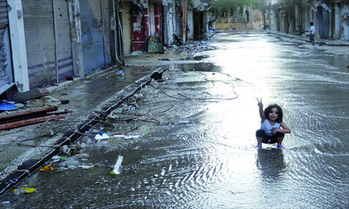 A handout image released by the Syrian opposition's Shaam News Network on Monday shows a girl flashing the sign for victory in a destroyed street flooded with water in the restive central city of Homs. Photo: AFP  