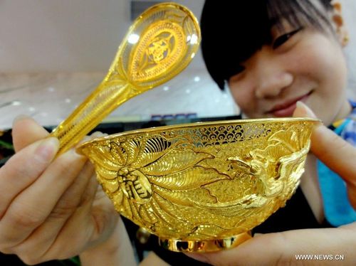 A staff member shows a set of gold tableware at a gold store in Jinan, capital of east China's Shandong Province, August 20, 2012. The set of tableware sells at 14,000 RMB ($2200). Photo: Xinhua