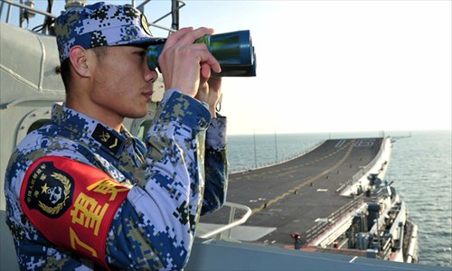 A People's Liberation Army Navy crewman looks through binoculars aboard the <em>Liaoning</em>, China's first aircraft carrier, on Friday. The <em>Liaoning</em> docked at a military port in Sanya, South China's Hainan Province on Friday. Photo: Xinhua