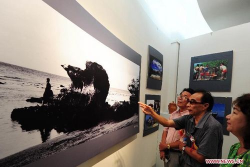 Visitors look at photos presented in an exhibition of documentary photography for Sansha City in Sanya, South China's Hainan Province, August 5, 2012. A total of 117 photos from 2002 to 2008 by Huang Qiqing, vice president of Sanya Photographers Association, were displayed during the exhibition. Photo: Xinhua