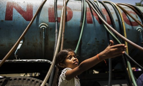 An Indian girl gestures as residents fill water containers from a government water supply truck in New Delhi on Wednesday. With temperatures hovering around 45 C, residents are struggling as Delhi has been going through a severe water shortage for the past few days after the upper Ganga Canal was shut for repairs. Photo: AFP