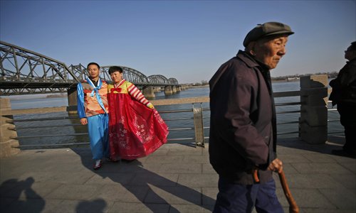 An elderly man walks in front of Chinese tourists dressed in Korean traditional costumes posing for photos at the Sino-Korean Friendship Bridge on April 7. Photo: CFP