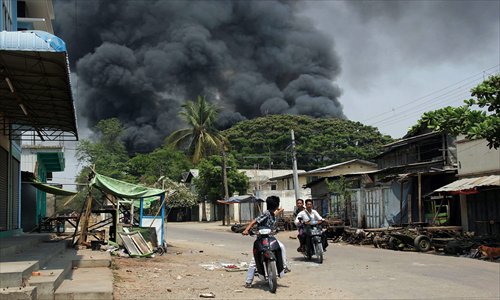 Black smoke rises from burning buildings as residents ride motorcycles in a street in riot-hit Meiktila, central Myanmar on Thursday.  At least 10 people have been killed in riots in central Myanmar, a local MP said, in the worst communal violence since Buddhist-Muslim clashes in western Rakhine state last year. Photo: AFP